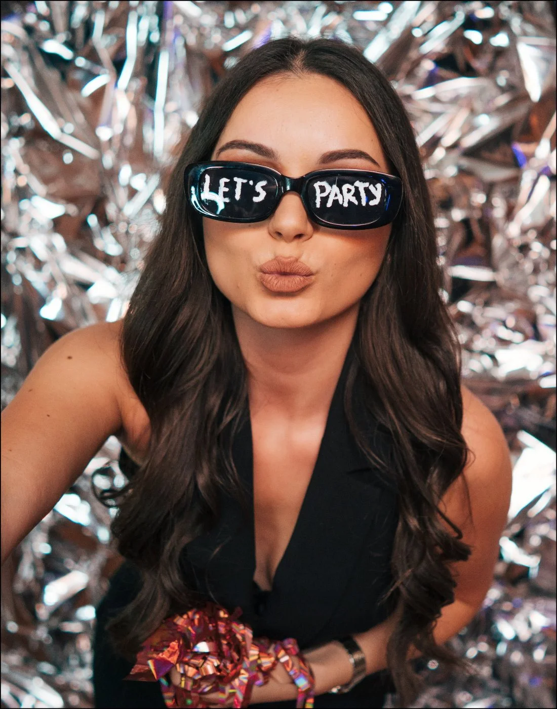 Frau mit Let's-Party-Brille vor Glitzerhintergrund